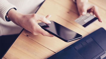 mani impugnano spartphone e carta di credito vicino a PC